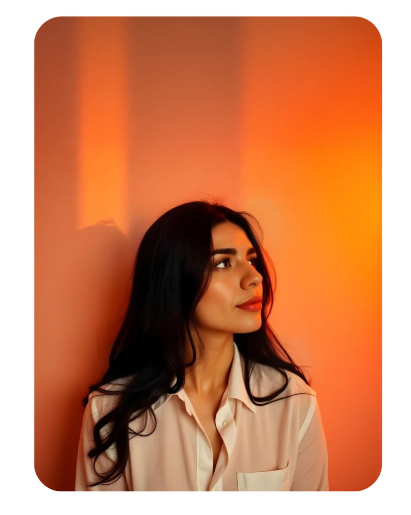 Foto de perfil, mujer joven con cabello largo y oscuro, sentada frente a una pared con luz cálida y tenue, mirando ligeramente hacia arriba.